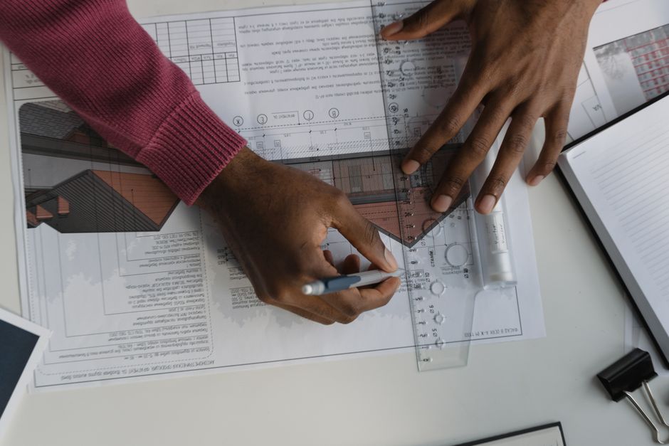 Architect sketching on blueprints with ruler at desk, designing a building layout.
