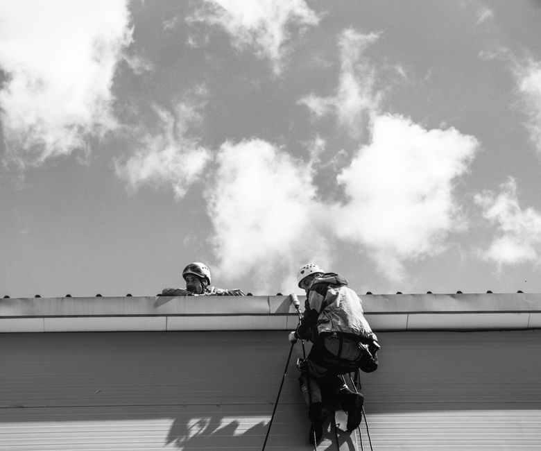 Two workers in safety gear inspecting rooftop against cloudy sky.